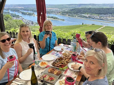 Friends toasting with red wine over a hearty snack platter on a terrace overlooking vineyards and the Rhine