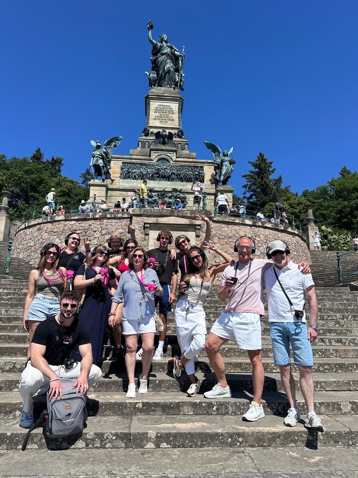 Group of people with headphones and wine glasses posing on the steps of the Niederwald Monument.