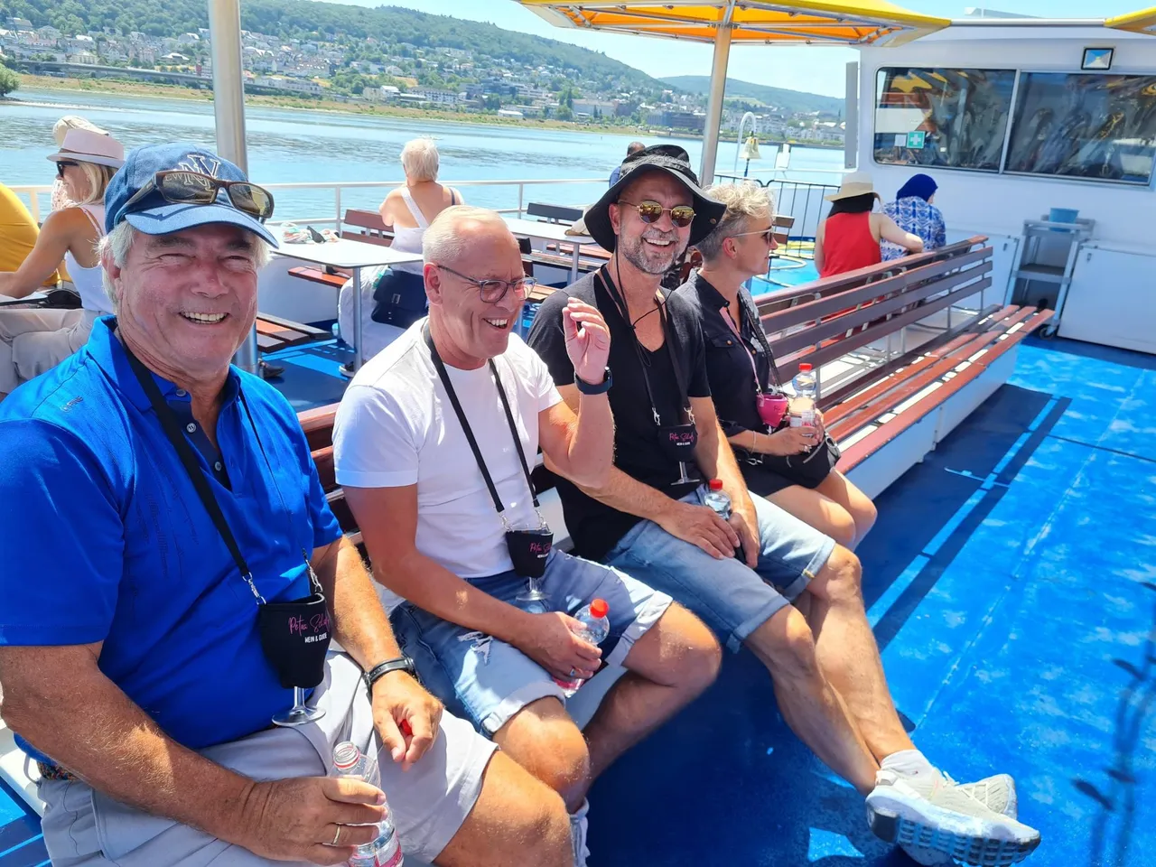 Laughing group of people with wine glasses in neck holders on the sunny deck of a Rhine boat