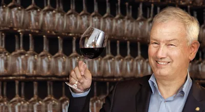A man holding a glass of red wine in front of a shelf with lots of empty wine glasses