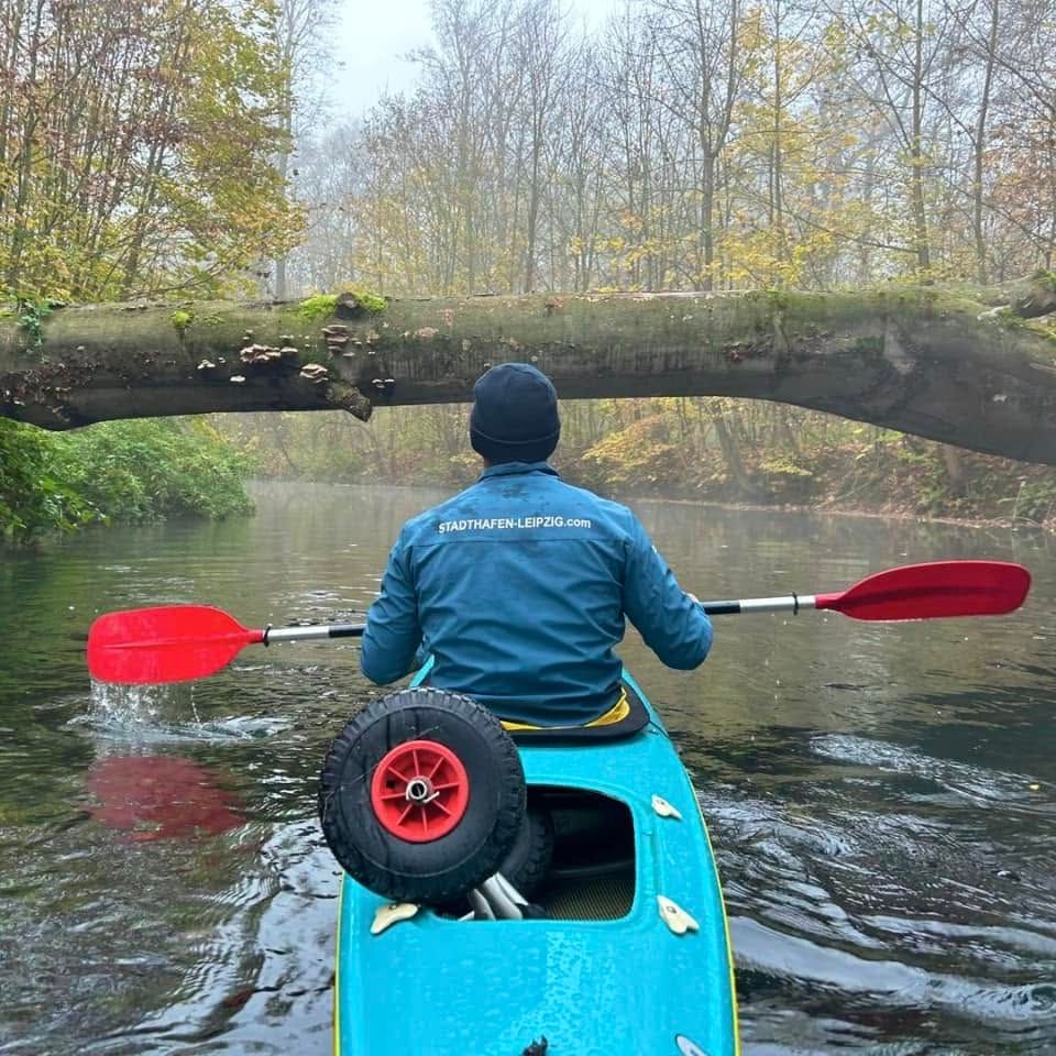 Paddler in a turquoise canoe gliding along a misty river through a late-autumn floodplain forest in Leipzig