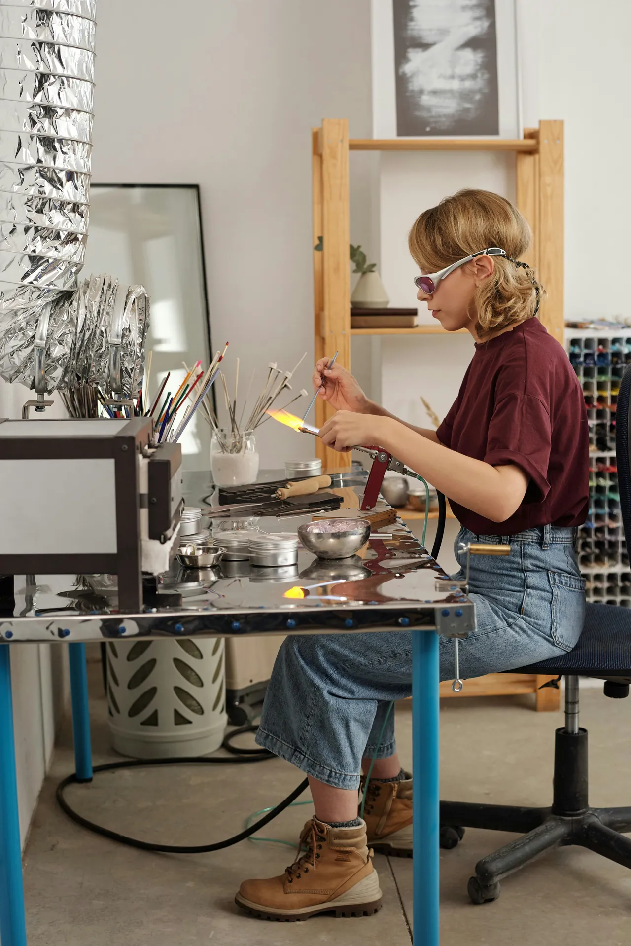 Woman wearing safety glasses lampworking glass rods over a flame in a studio