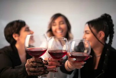 Three smiling women holding up glasses of red wine