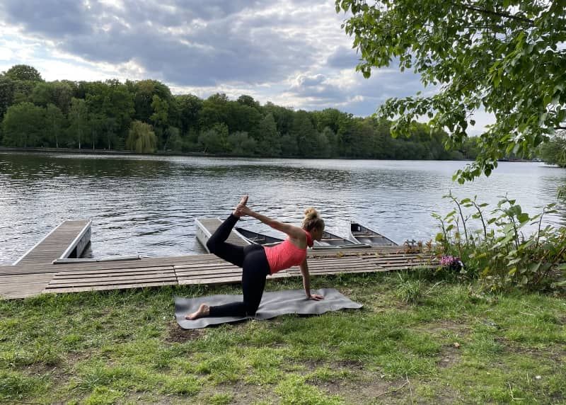 Woman holding a yoga pose on a wooden jetty by the water during a yoga canoe tour in Berlin