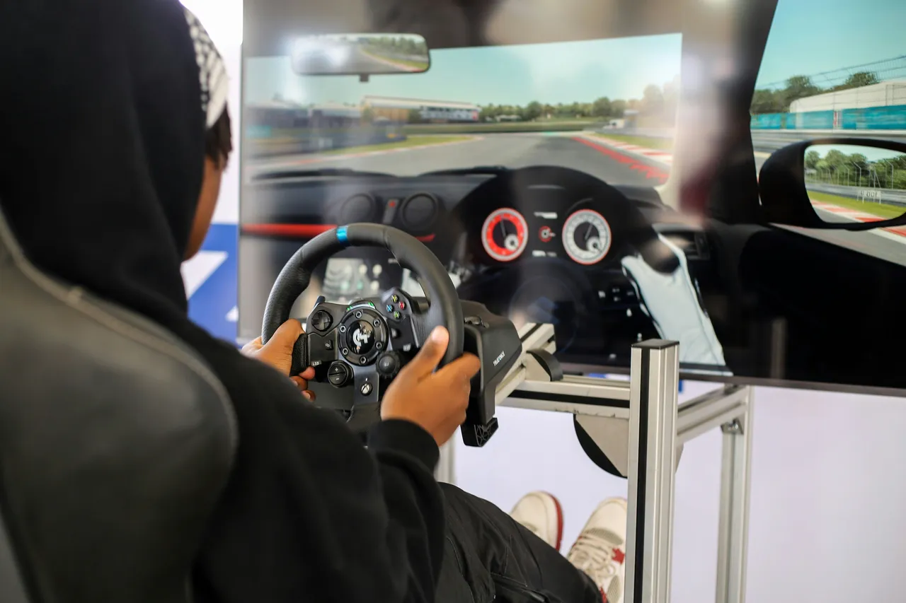 A young man smiling while sitting in the driver's seat of a car, holding the steering wheel with both hands.